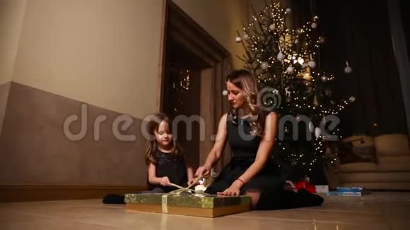 妈妈和女儿坐在圣诞树下打开礼物女孩解开礼物的丝带总体计划视频的预览图