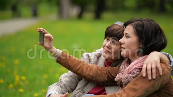在公园野餐快乐的一家人用手机拍下自己的照片成年女儿与母亲视频的预览图