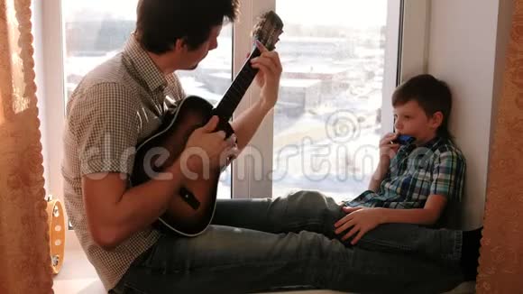 演奏乐器爸爸在弹吉他儿子坐在窗台上弹口琴视频的预览图