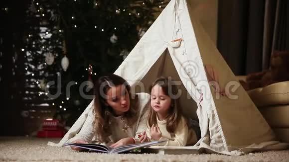 我的母亲和女儿穿着白色的毛衣读了一本童话故事和她躺在一个帐篷里视频的预览图