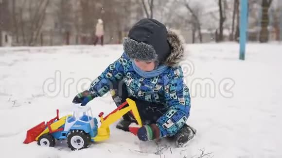 小男孩在玩具车里玩雪地里的拖拉机视频的预览图