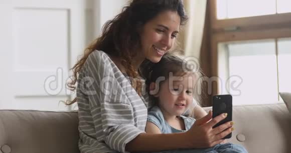 可爱有趣的小女孩和妈妈一起玩智能手机视频的预览图