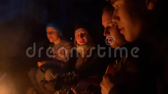 夜晚森林里篝火前的朋友用吉他唱歌视频的预览图