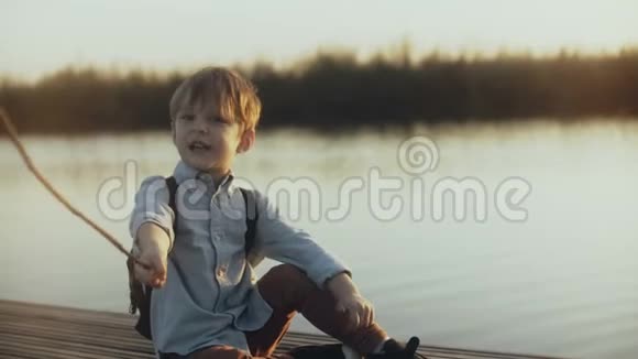 可爱的男孩孩子坐在日落湖附近的棍子高加索儿童在码头上玩愤怒的野生海盗的肖像4K视频的预览图