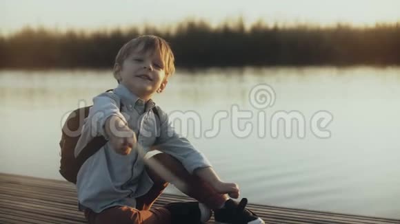 可爱的男孩坐在湖边码头上小白种人儿童谈话的肖像愉快地看着镜头4K视频的预览图
