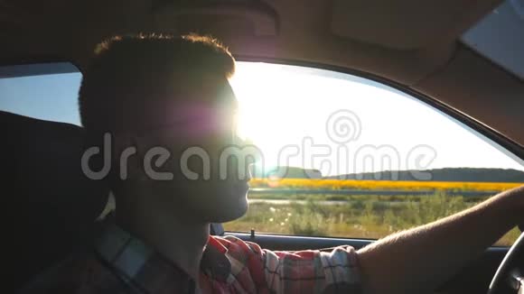 戴太阳镜的年轻人驾驶背景有太阳耀斑的汽车日落时分开车的帅哥视频的预览图