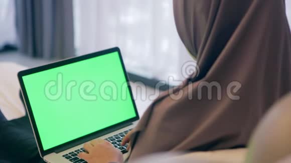 穆斯林妇女坐在绿色屏幕笔记本电脑上工作的后视图视频的预览图