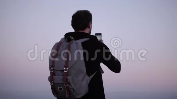 高加索人欣赏令人惊叹的山景慢动作兴奋的游客拍摄智能手机照片紫罗兰黄昏的天空视频的预览图