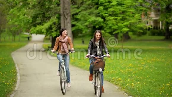 在春天里骑着自行车微笑的布鲁内特正在公园里骑马两名穿著夹克及视频的预览图
