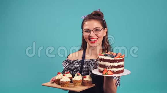 情绪化的金发女孩糕点厨师拿着一个大蛋糕在演播室里对着镜头微笑视频的预览图