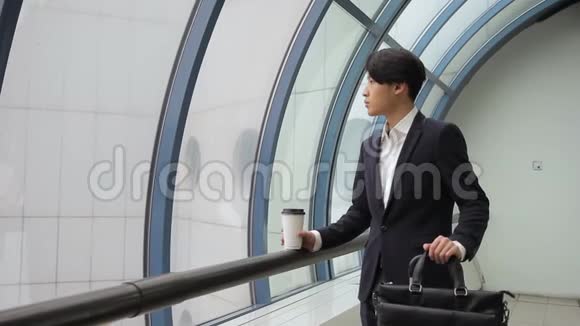 穿着夹克衫的亚洲男性喝着咖啡在雨中看着窗户视频的预览图
