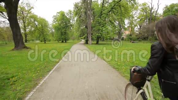 春天公园里穿着漂亮的夹克和骑自行车的牛仔裤后视图相机在运动视频的预览图