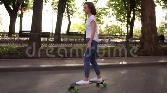 公园日出时穿着蓝色牛仔裤和白色运动鞋的年轻女人在滑板滑板上的腿慢镜头视频的预览图