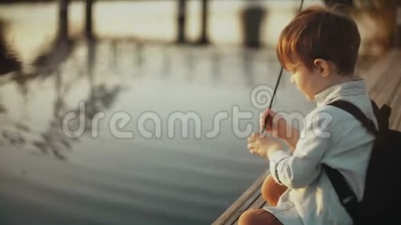 可爱的白人男孩在湖边玩棍子小可爱的孩子在码头上背包快乐的童年4K视频的预览图