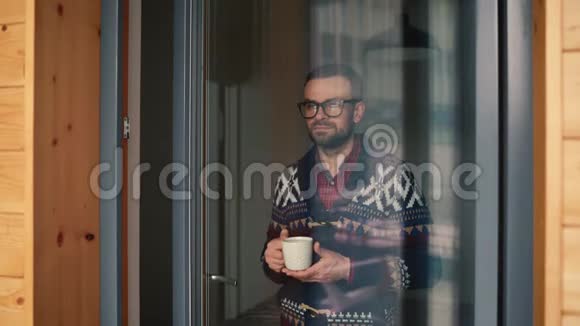 男人在窗边喝茶或喝咖啡透过玻璃看视频的预览图