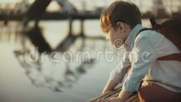 可爱的欧洲男孩在码头上玩湖水小男孩带背包探索夏天的自然4K特写视频的预览图