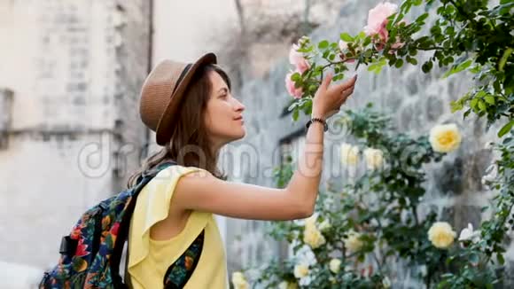 戴帽子的漂亮女人走在街上在春天的户外女孩游客在花园里嗅花视频的预览图