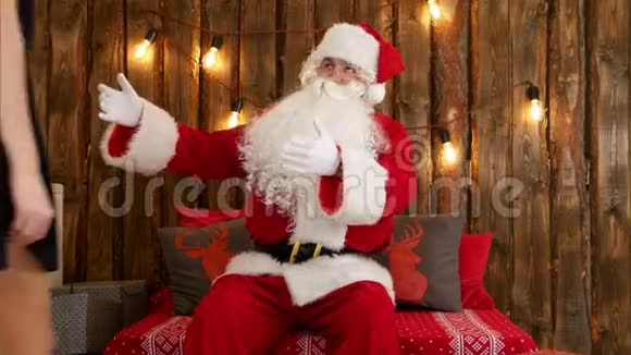 漂亮的黑发少女坐在圣诞老人的膝上向她诉说圣诞祝福视频的预览图