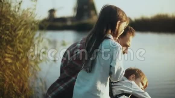 快乐的高加索家庭坐在宁静的日落湖附近单身父亲和两个孩子在一起度过快乐的时光4K特写视频的预览图
