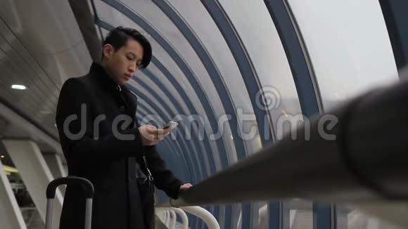 亚洲人在口袋里拿起电话带着手提箱去车站候车室视频的预览图