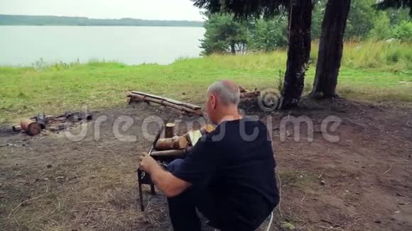 河岸上的一个人坐在烧烤处用一条鱼把烤架翻过来视频的预览图