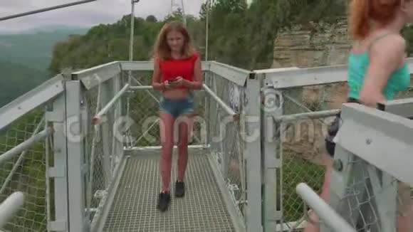 镜头跟随两位年轻的白种人运动妇女在高山上的吊桥上行走视频的预览图
