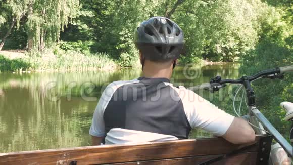 一个骑自行车的人夏天在公园里休息他坐在池塘附近的长凳上视频的预览图