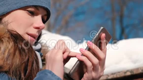 女人坐在冬季公园的手机上浏览网页特写的脸视频的预览图