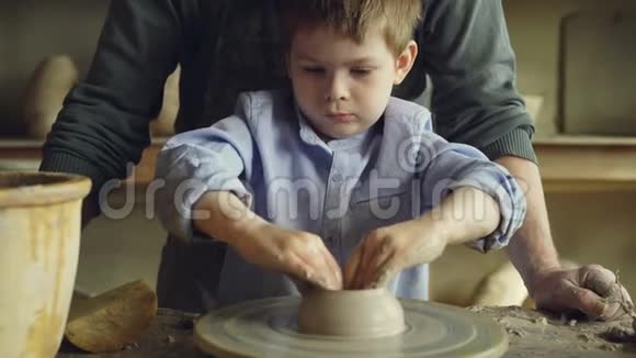 当他的祖父有经验的雕刻家是一个严肃的小男孩他轮上制作粘土图形的特写镜头视频的预览图