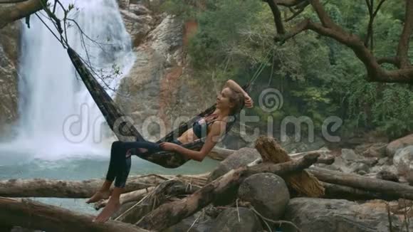 在瀑布附近的吊床上的金发女孩视频的预览图