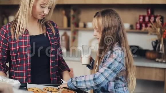 妈妈和女儿一起在厨房品尝新鲜出炉的圣诞巧克力饼干和牛奶视频的预览图