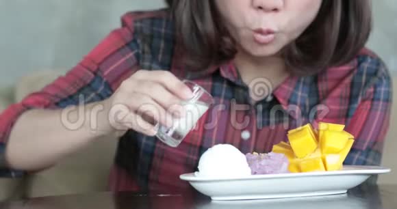 快乐的亚洲女人在芒果和糯米上倒入椰奶视频的预览图