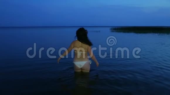 黄昏时穿着白色泳衣在湖中的年轻女子视频的预览图
