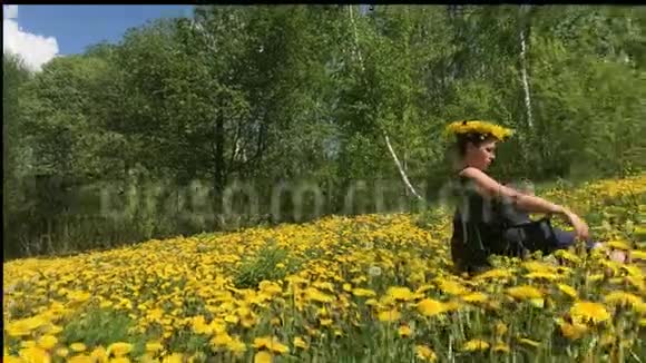 女孩坐在一片春草地上长满了开花的蒲公英在蒲公英叶脉的头上阳光明媚的春天视频的预览图