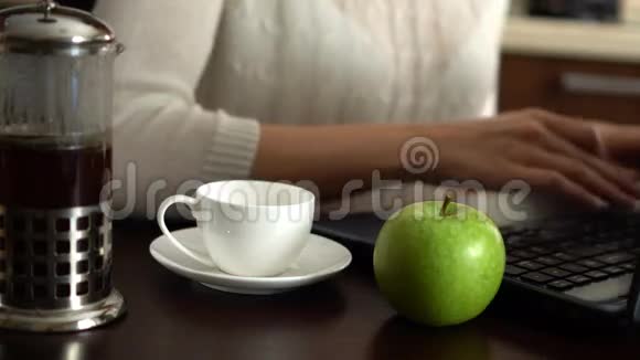 漂亮的年轻女人在家里厨房里用笔记本电脑倒一杯咖啡苹果在桌子上视频的预览图
