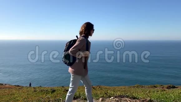 一个年轻的女人从山上的摄像机里走开了背景上的海洋视频的预览图