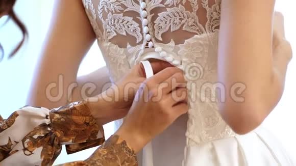 特写新娘费用新娘为婚礼穿衣服伴娘用丝带系上白色花边连衣裙婚礼视频的预览图