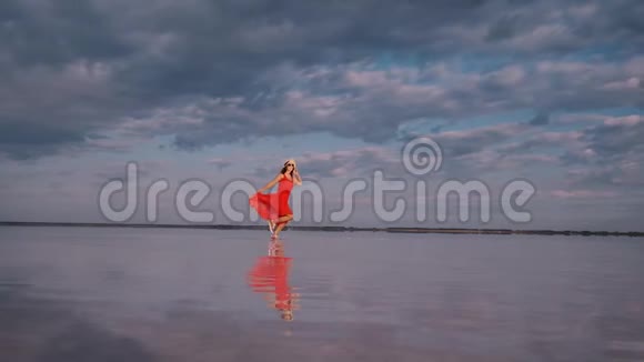 年轻女子穿着飘舞的裙子沿着一个盐湖奔跑那里的天空被反射视频的预览图