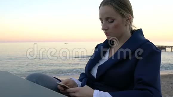 漂亮的女人坐在海滩咖啡馆的桌子上用手机发送信息视频的预览图