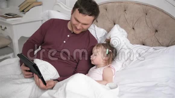 现代家庭在卧室消费周末一起放松小父亲和小女儿在用小玩意视频的预览图