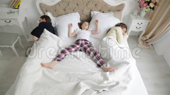 幸福的家庭正在白床上休息睡衣中睡着的母亲父亲和小女儿的肖像视频的预览图