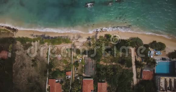 封闭空中拍摄的异国情调海岸度假房屋与棕榈树海浪洗可爱的海滩在阳光明媚的一天视频的预览图