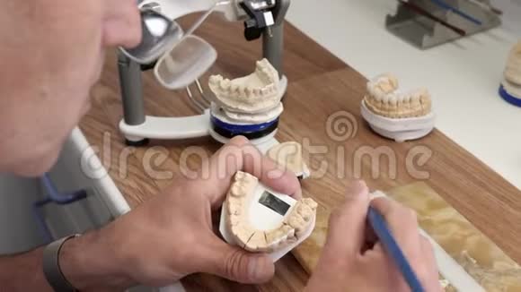 牙科技师在背景木制的工作场所用刷子将白色粉末涂在下巴模型上进行牙齿修复视频的预览图