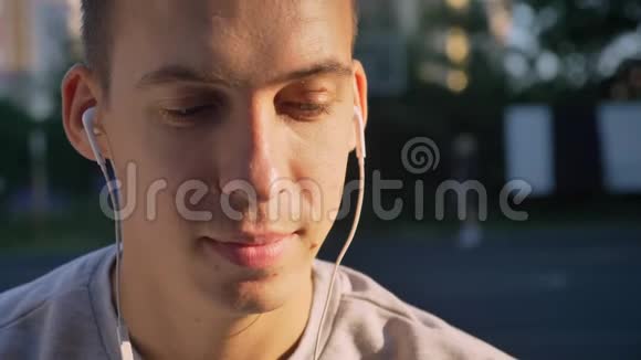 英俊的年轻人通过耳机听音乐看镜头人们在背景中演奏的肖像视频的预览图
