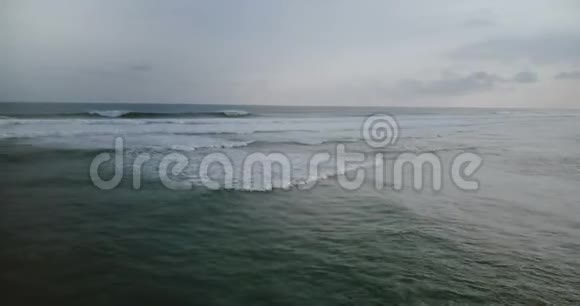 无人机左转露出大片深蓝色的海浪在多云的暴风雨天空下伴随着白色泡沫的碰撞视频的预览图