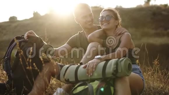 徒步旅行夫妇徒步旅行者在山上休息年轻女子和男子徒步旅行者坐在地上欣赏着风景微笑着快乐着视频的预览图