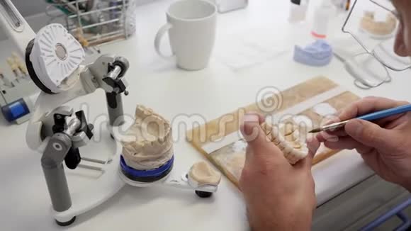 为病人制造牙科假体戴眼镜的专家在工作场所给人造牙齿涂上搪瓷视频的预览图