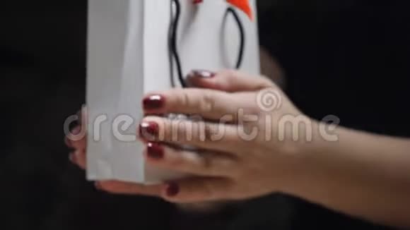 女性手指的特写展示了带有红色丝带和蝴蝶结的纸礼盒以女人的身份打开一个礼品盒视频的预览图