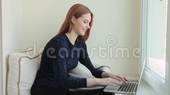 漂亮的年轻女性在家坐在窗台上用笔记本电脑在社交网络上交流视频的预览图
