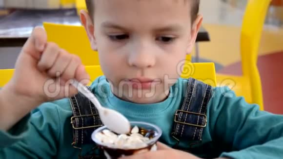 可爱的小男孩穿着商人西装午餐时在餐馆里匆忙吃冰淇淋视频的预览图